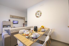 Un comedor moderno con una mesa de madera dispuesta para cuatro personas, un sofá y un televisor montado en la pared.
