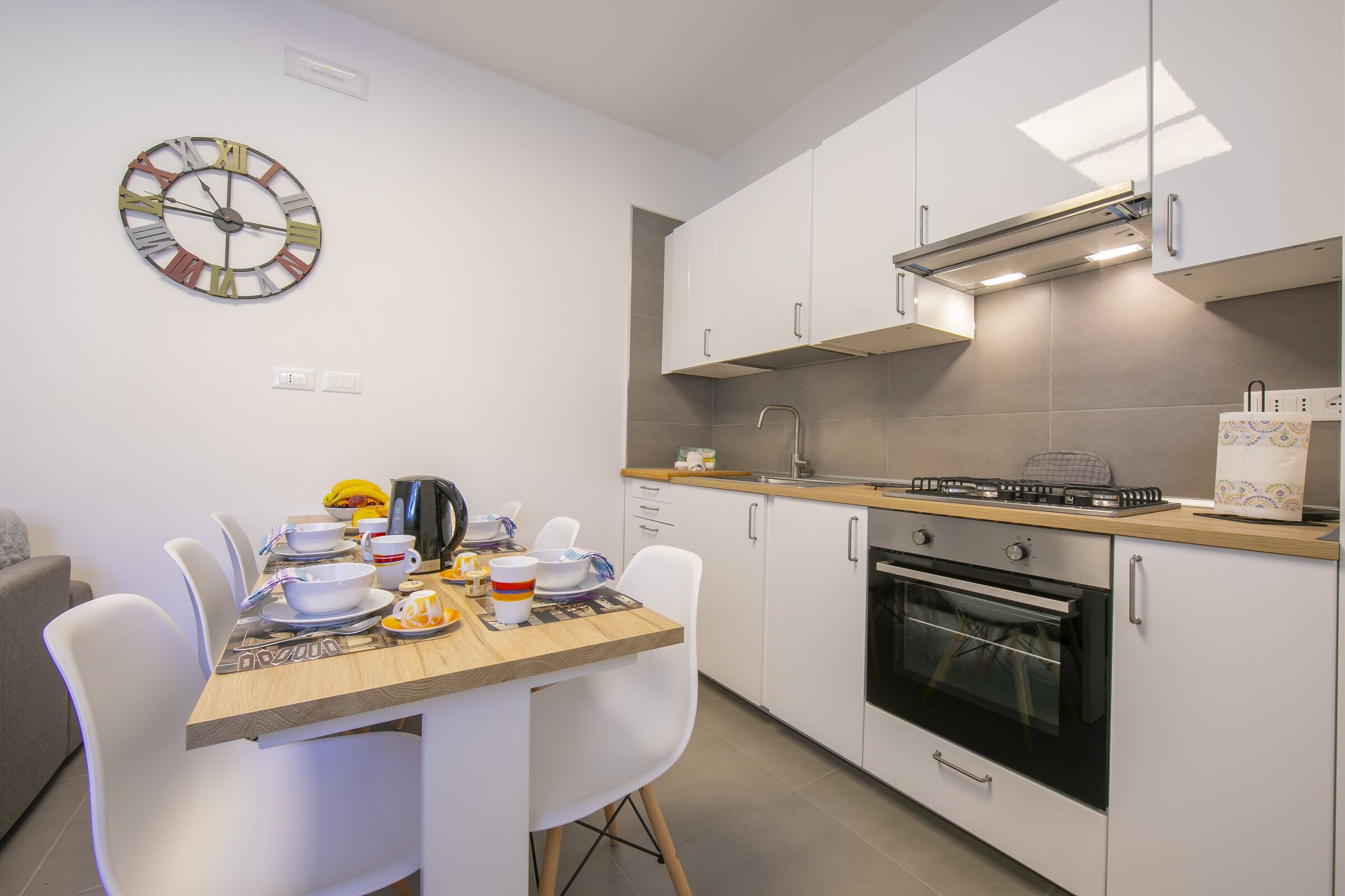 A modern kitchen with white cabinets, a built-in oven, and a dining area with a wooden table and white chairs.