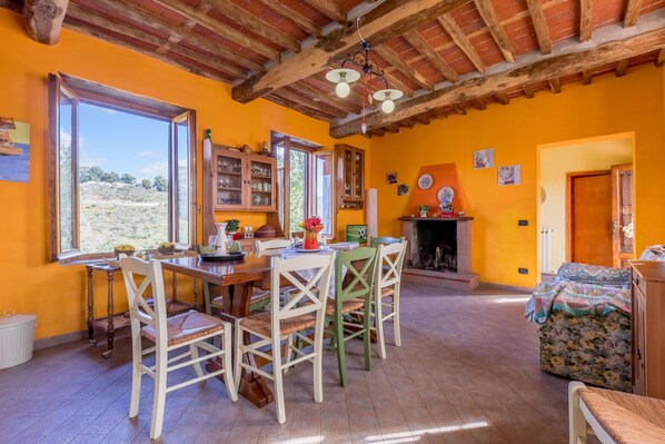 A dining area with a wooden table and chairs, a fireplace, and large windows with a view of the outdoors.