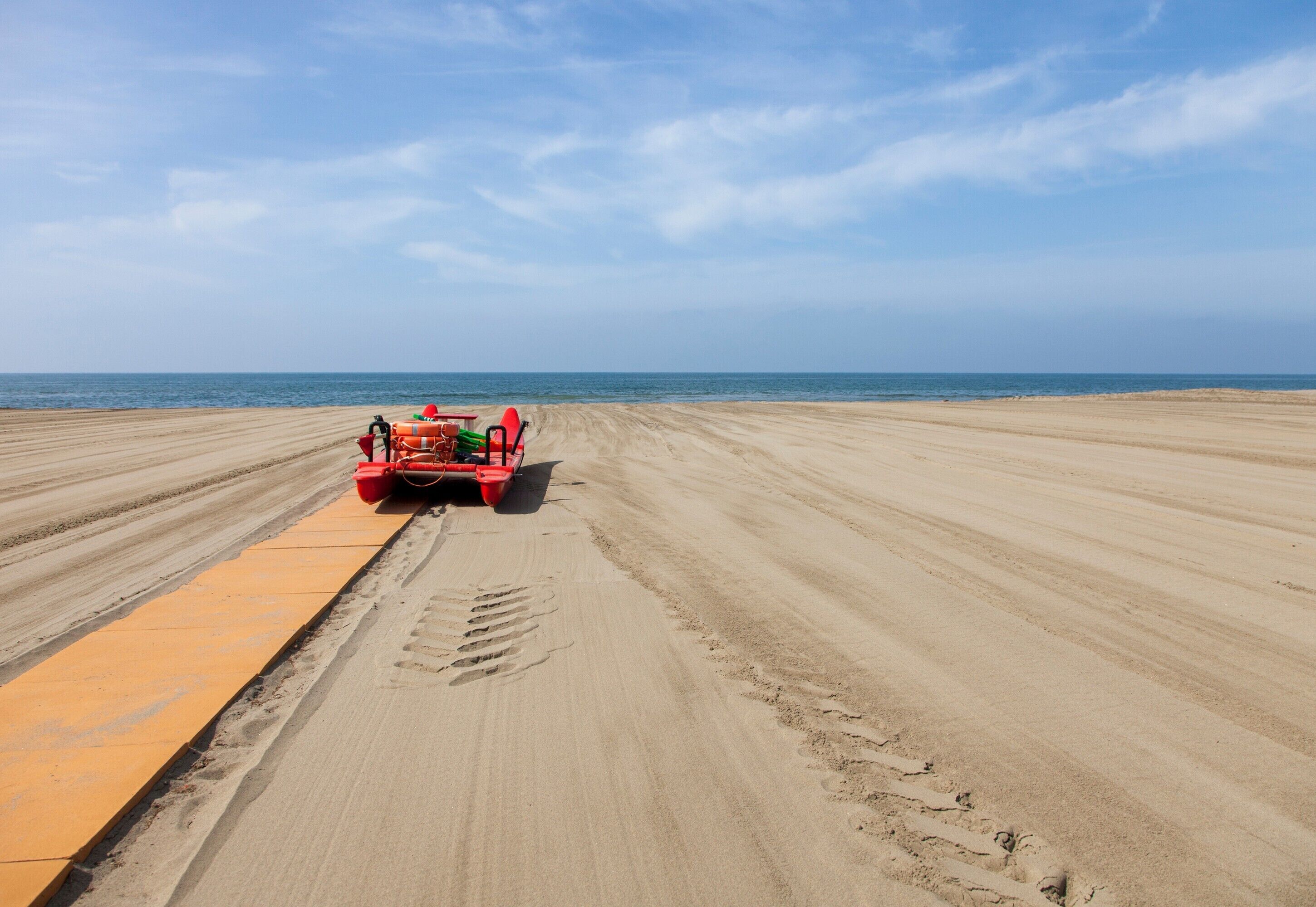 A beach with a red vehicle and a yellow safety barrier.