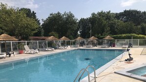 Una piscina rectangular con una escalera metálica, rodeada de sillas de descanso y sombrillas de paja.