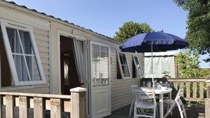 Une terrasse en bois avec une table et des chaises, un parasol bleu et un bâtiment blanc aux fenêtres ouvertes.
