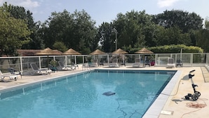 Une piscine entourée d’une clôture et d’arbres, avec des chaises longues et des parasols.