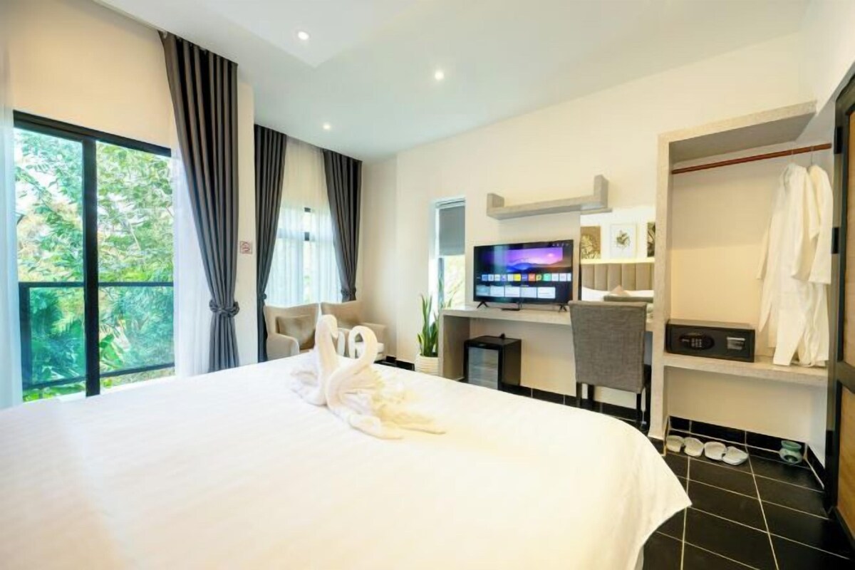 A hotel room with a bed, a TV, a desk, a chair, a wardrobe, and a large window with curtains.