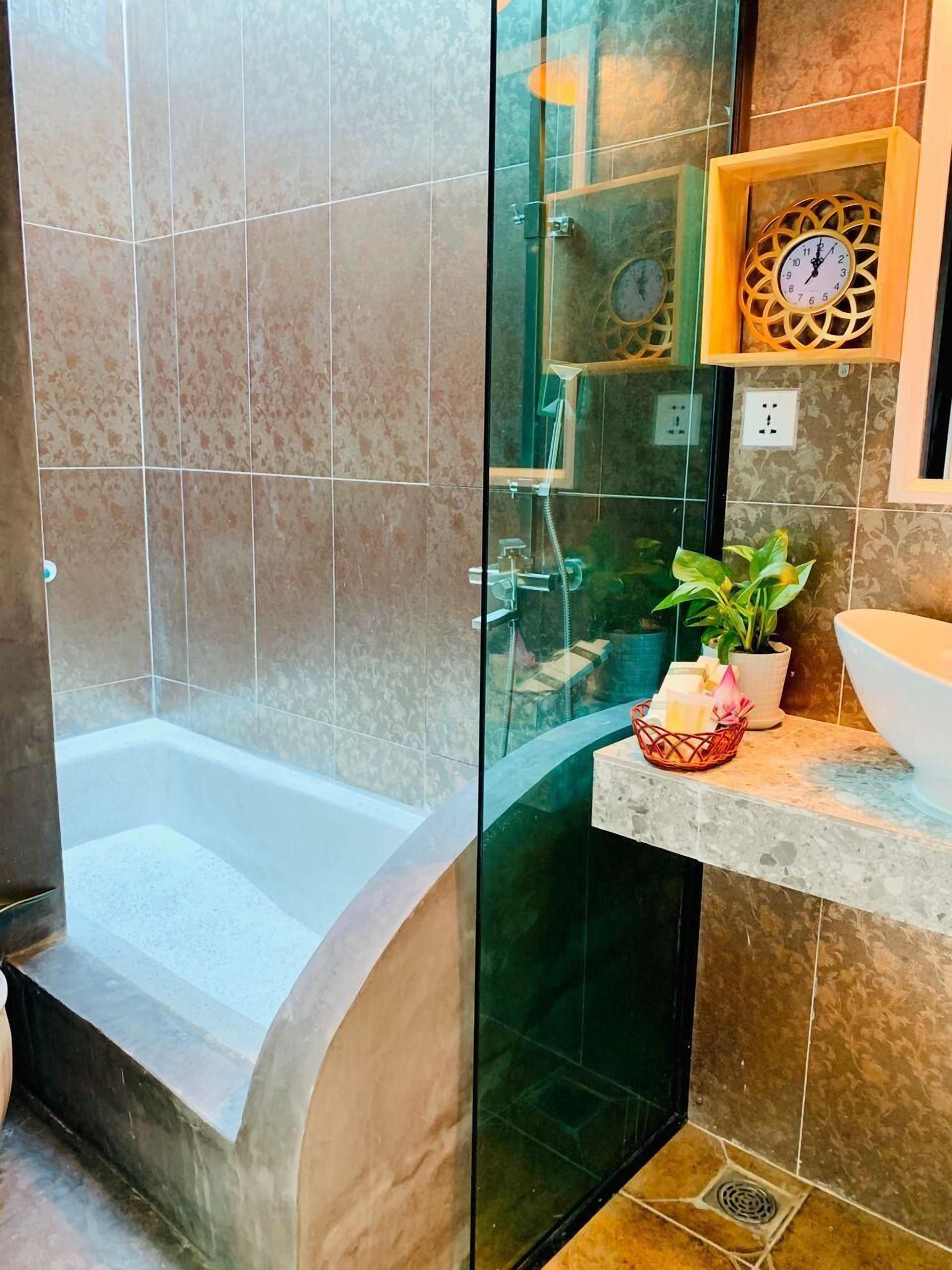 A modern bathroom with a glass-enclosed shower, a bathtub, and a sink area with decorative items.