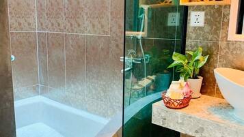 A modern bathroom with a glass-enclosed shower, a bathtub, and a sink area with decorative items.