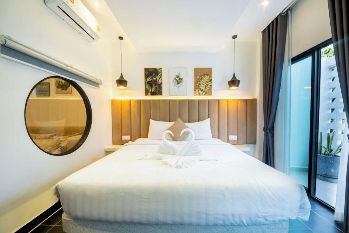Quarto de hotel moderno com uma cama grande, um espelho redondo e vista para o verde lá fora.