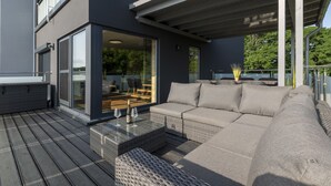 A modern outdoor living area with a sofa, a table, and a glass door leading to an indoor space. - Traumhaus 6 Personen,150m²,sauna,wanne,kamine,terrassen,garten,grill,sky TV (Neukieritzsch)