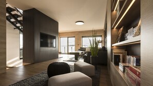 A modern living room with a large flat-screen TV, a staircase, and a bookshelf with books and decorative items. - Traumhaus 6 Personen,150m²,sauna,wanne,kamine,terrassen,garten,grill,sky TV (Neukieritzsch)