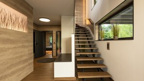 A modern staircase with wooden steps and a glass railing, leading to a landing with a large window overlooking greenery. - Traumhaus 6 Personen,150m²,sauna,wanne,kamine,terrassen,garten,grill,sky TV (Neukieritzsch)