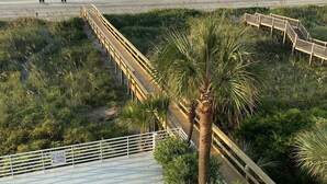 Vista de la playa con un paseo marítimo de madera, una piscina y un letrero que indica aguas poco profundas.