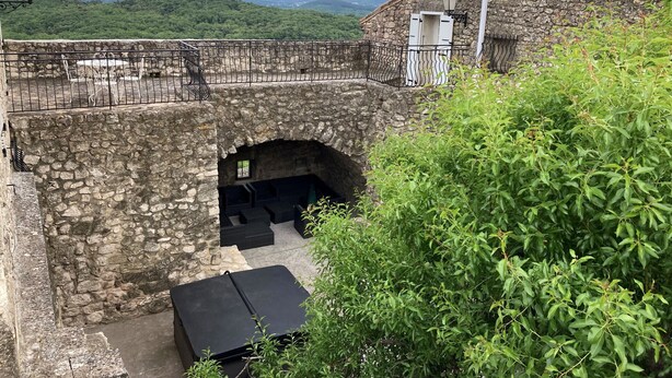 Un bâtiment en pierre doté d’un balcon, d’une petite arche et d’une table avec des chaises.