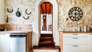 Une cuisine équipée d’un lave-vaisselle, de meubles en bois, d’une horloge et d’un mur en pierre rustique.