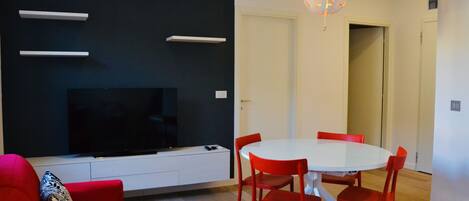Una sala moderna con un televisor de pantalla plana, una mesa de comedor blanca con sillas rojas y una pared de acento negra.