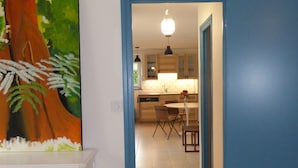 A hallway leading to a kitchen with a dining area, a white dresser, and a painting on the wall.