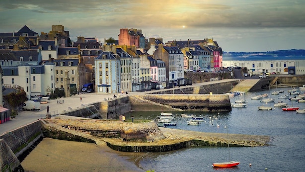 A coastal town with historic buildings, a harbor with boats, and a fortified wall.
