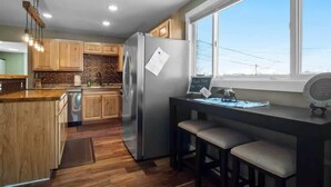Una cocina moderna con armarios de madera, un refrigerador de acero inoxidable, una isla integrada con taburetes y una ventana que ofrece vistas.