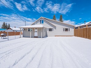 A single-story house with a covered porch, a fenced yard, and a clear blue sky.