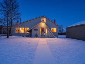 A two-story house with a snow-covered driveway and a welcoming sign.