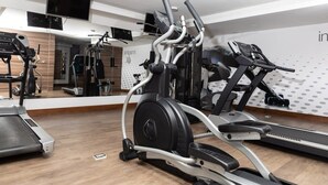 Un gimnasio con máquinas de cardio, un espejo grande y un televisor en el techo.