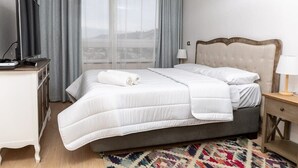 Habitación de hotel con cama, televisión, escritorio y vistas a un paisaje urbano por la ventana.