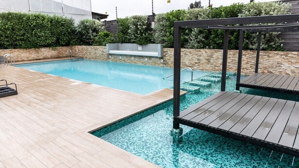 Una piscina con cubierta de madera y un muro de piedra al fondo.