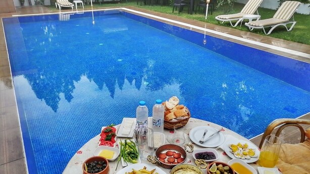 Desayuno junto a la piscina con una mesa llena de comida y bebidas, rodeada por una piscina y sillas de descanso.