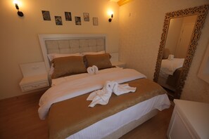 A neatly made bed with a headboard, a bedside table, a mirror with an ornate frame, and wall-mounted lights.