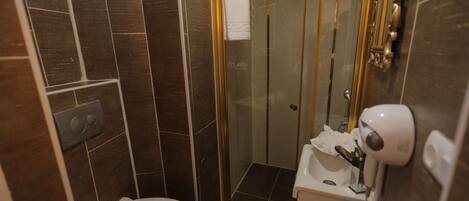 Un baño moderno con inodoro, cabina de ducha de vidrio y lavamanos con secador de pelo.