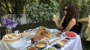 Una mesa montada al aire libre con diversos alimentos, como pan, queso y frutas.
