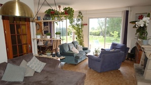 A living room with a sofa, armchairs, and a coffee table. There are plants and a bookshelf. - Quiet house for 8 near the beach (Locmariaquer)