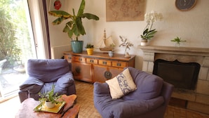 A cozy living room with two armchairs, a wooden cabinet with decorative items, and a fireplace. - Quiet house for 8 near the beach (Locmariaquer)
