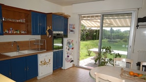 A kitchen with blue cabinets, a white refrigerator, and a dining table with fruit. - Quiet house for 8 near the beach (Locmariaquer)