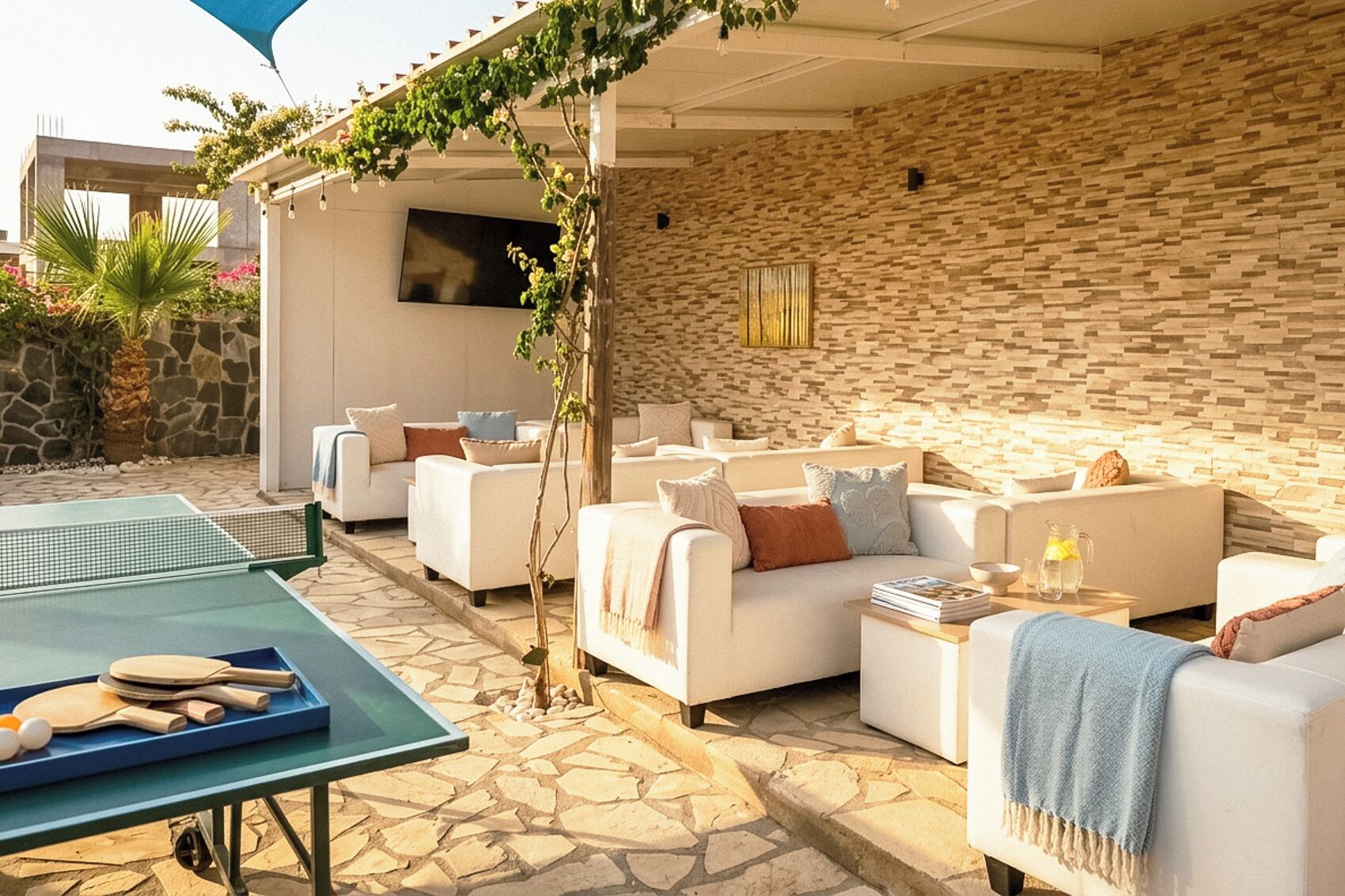An outdoor seating area with white sofas, a ping pong table, and a stone wall.