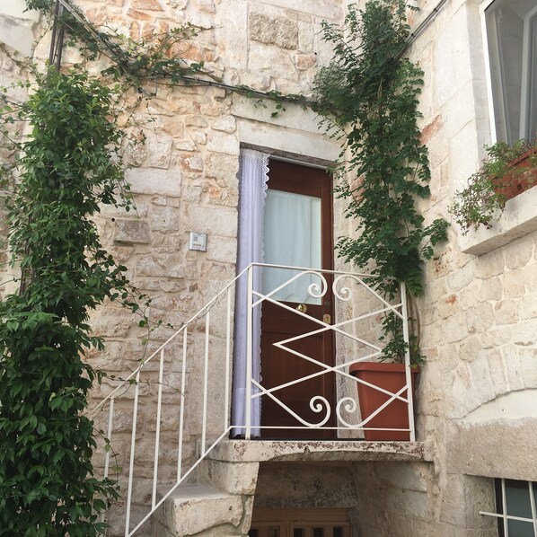 A stone building with a balcony featuring a wrought iron railing and a window with a curtain.