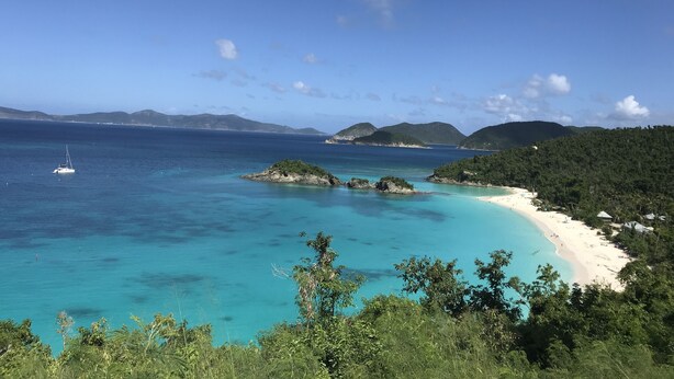 Un paisaje costero con playa, aguas azul turquesa y un velero.