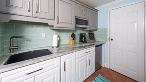 Una cocina con armarios blancos, un microondas de acero inoxidable y un lavamanos.