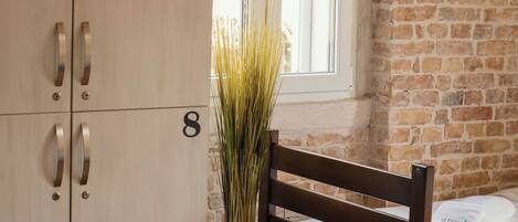 Una habitación con una cama de madera, una silla de madera, un armario de madera, una planta en maceta y una ventana con vistas al exterior.