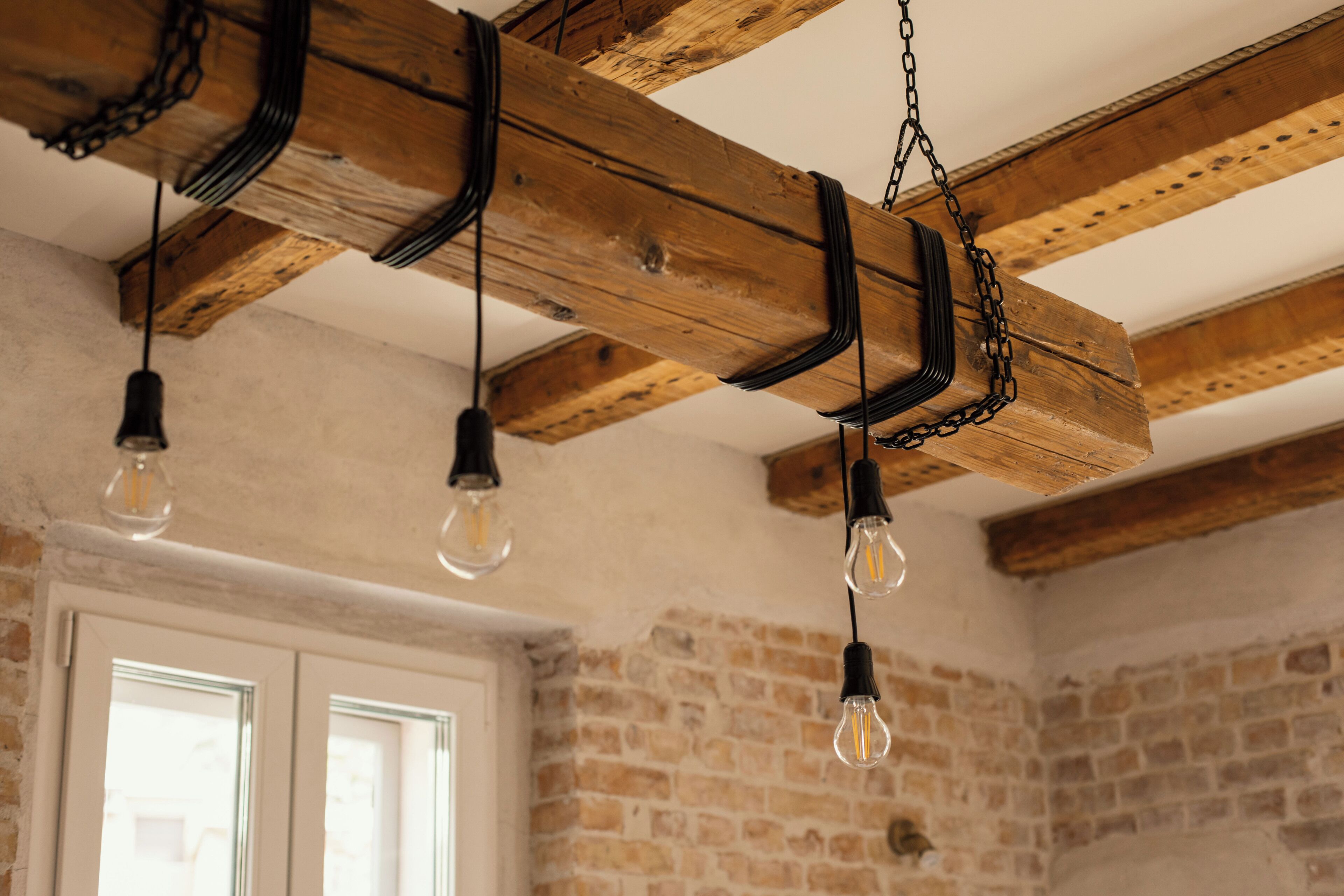 A room with exposed wooden beams, hanging light fixtures, and a brick wall.