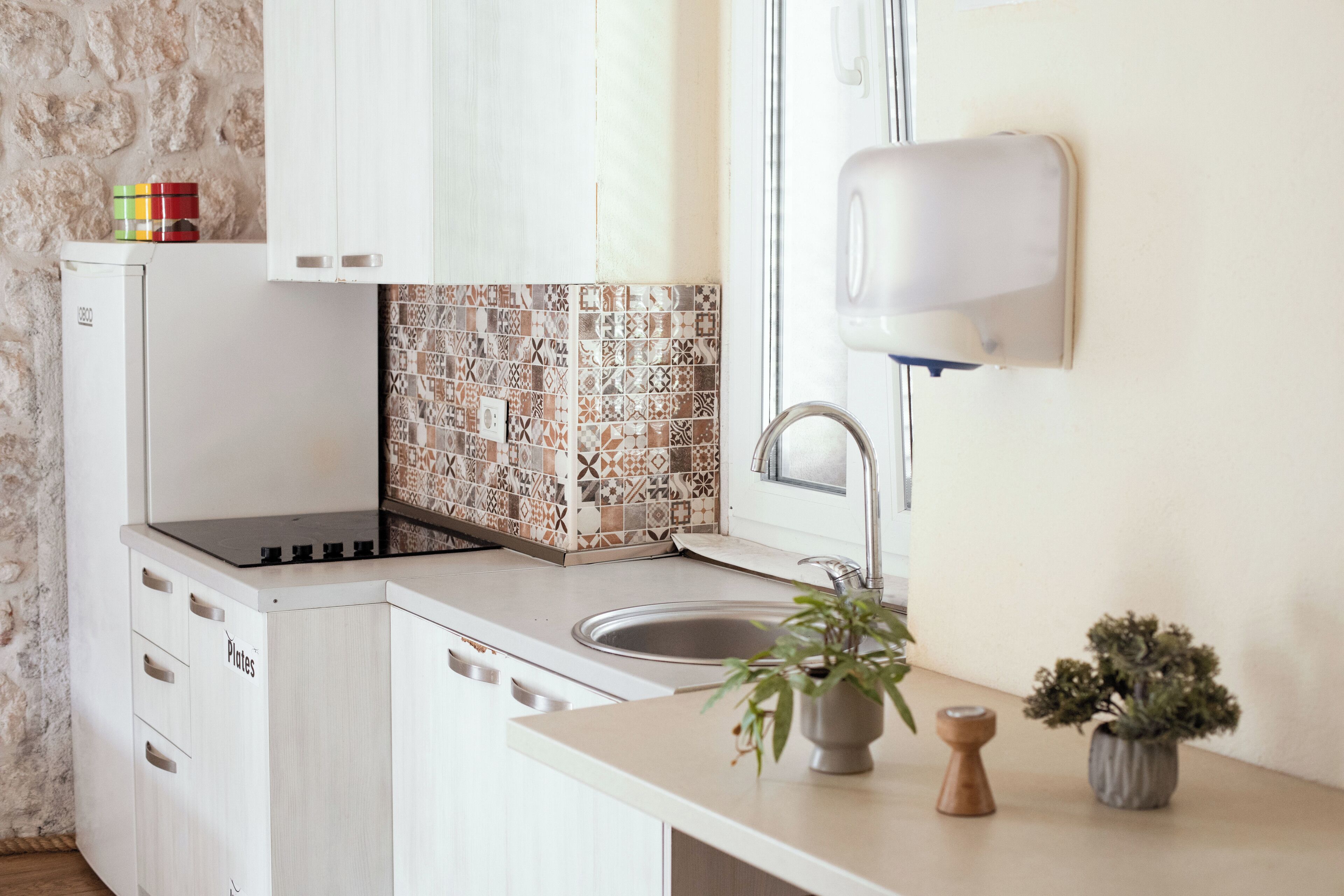 A kitchen with white cabinets, a tiled backsplash, a sink, a stove, and a potted plant.
