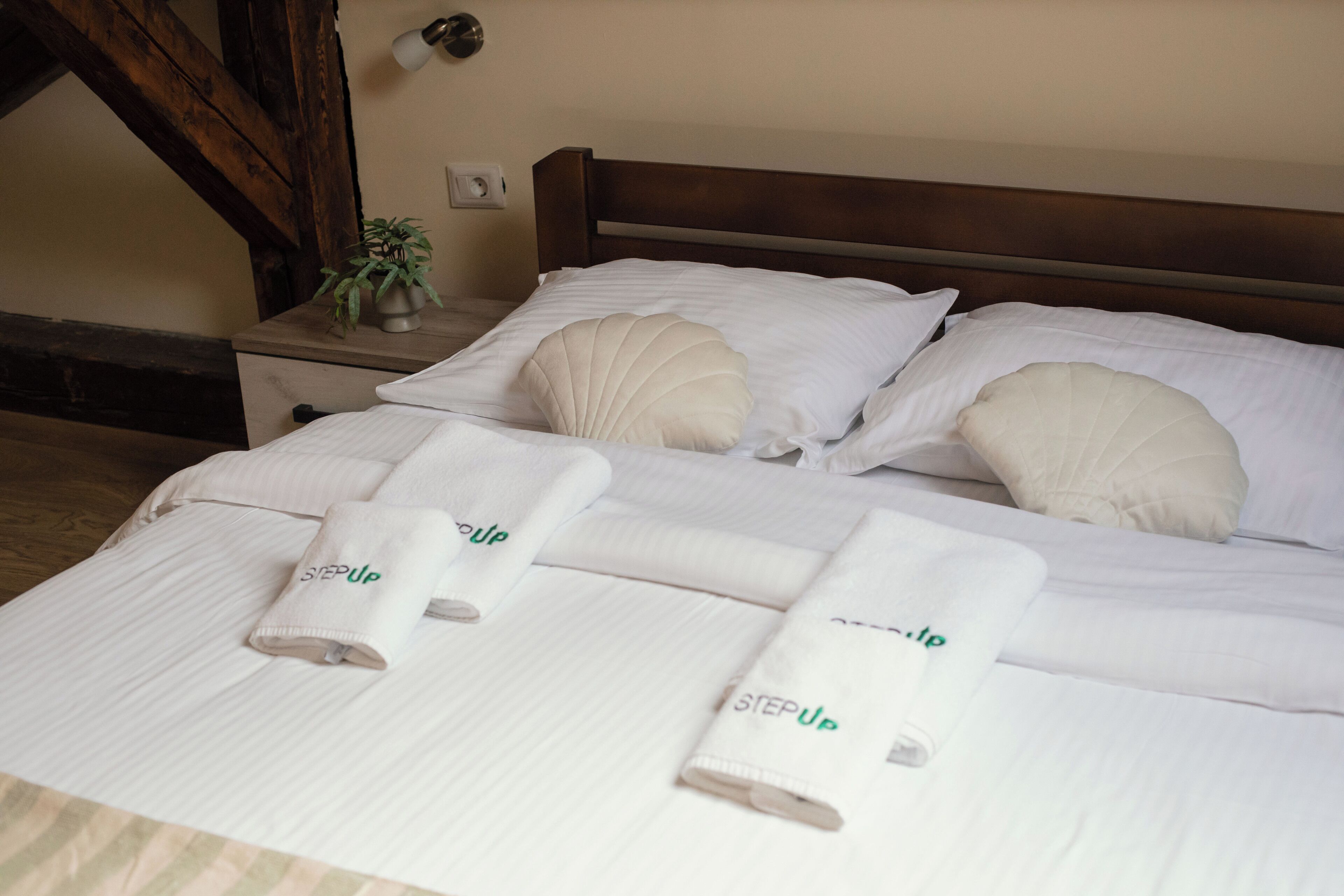 A neatly made bed with white linens and pillows, a bedside table with a plant, and a wall socket.