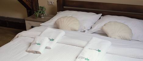 A neatly made bed with white linens and pillows, a bedside table with a plant, and a wall socket.