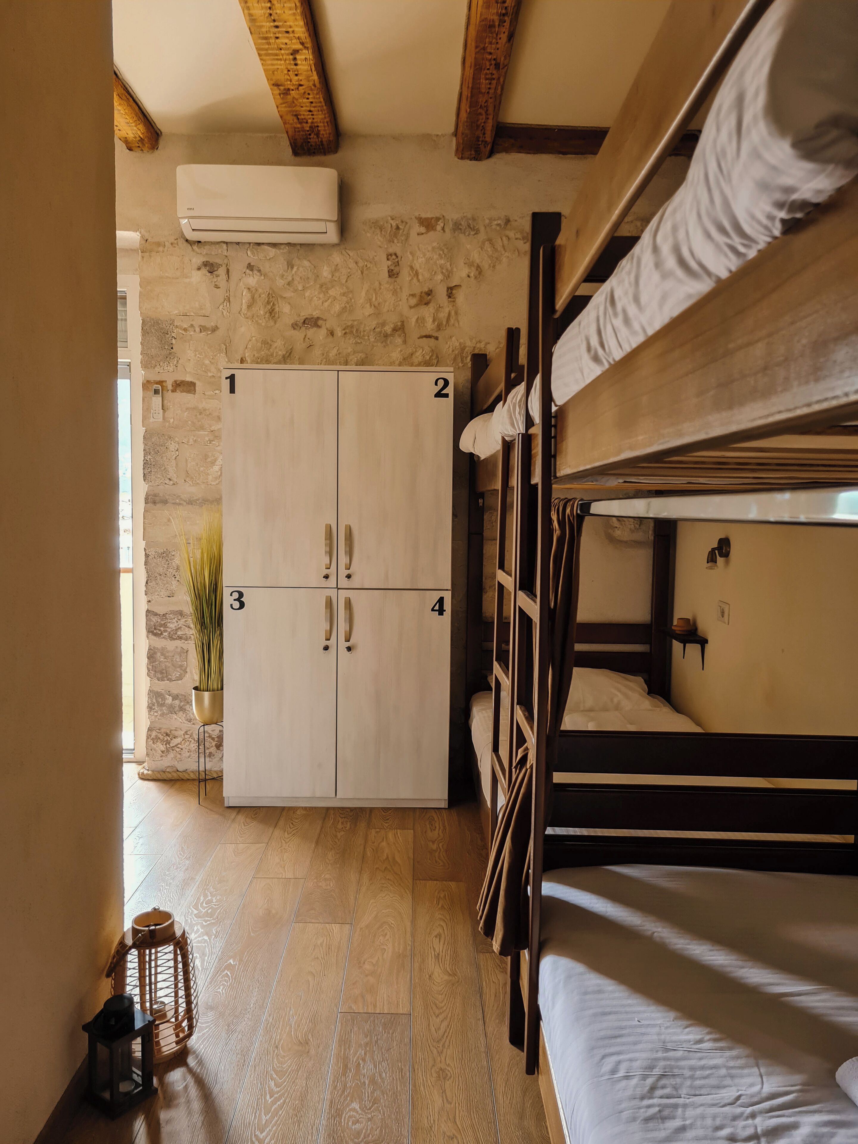 A bunk bed room with a stone wall, wooden beams, and a wardrobe with four doors.
