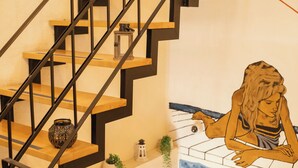 Una escalera con escalones de madera y barandillas negras, un farol decorativo y un mural en la pared.