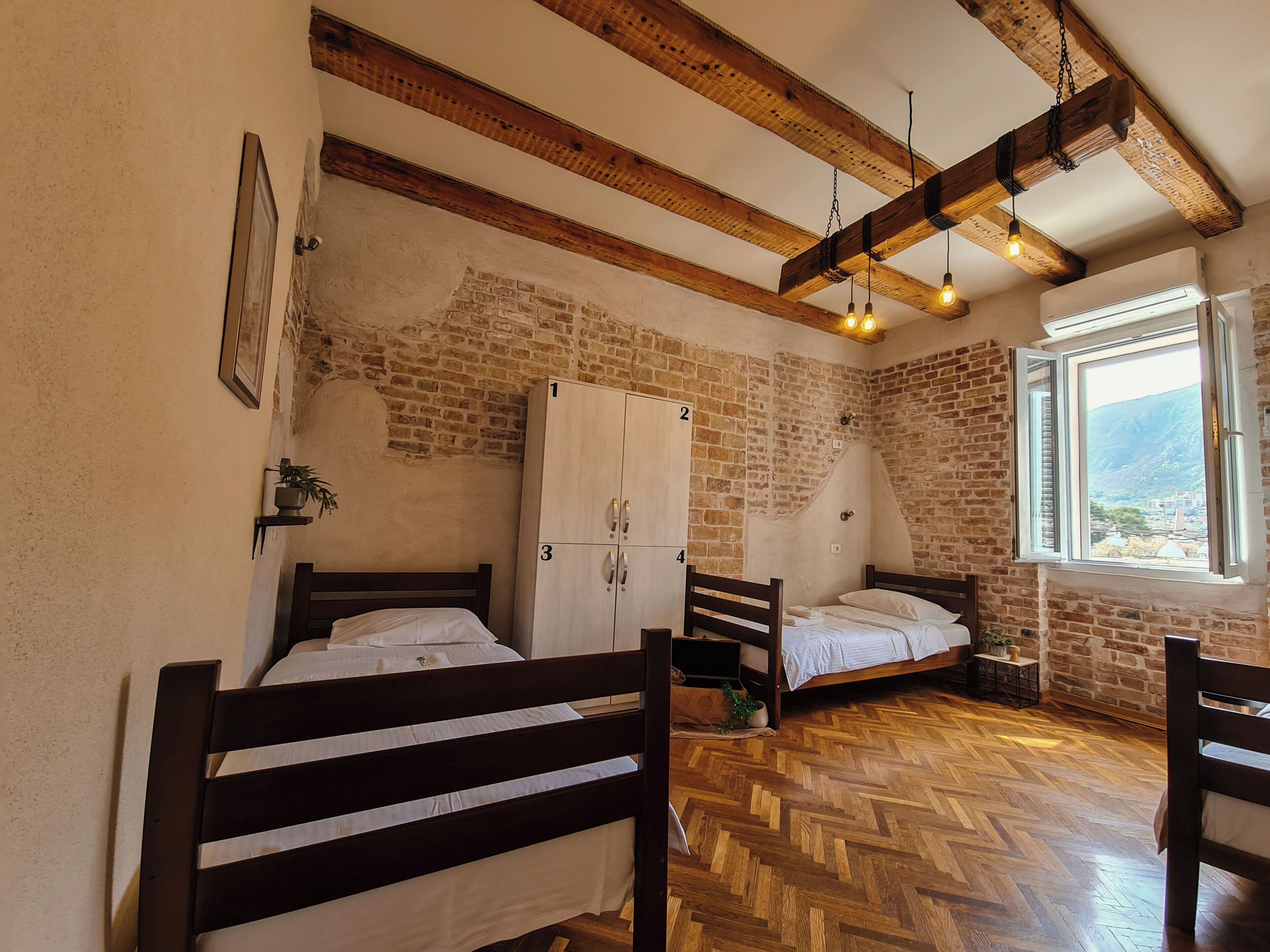Una stanza con due letti in legno, una parete in mattoni e una finestra vista.