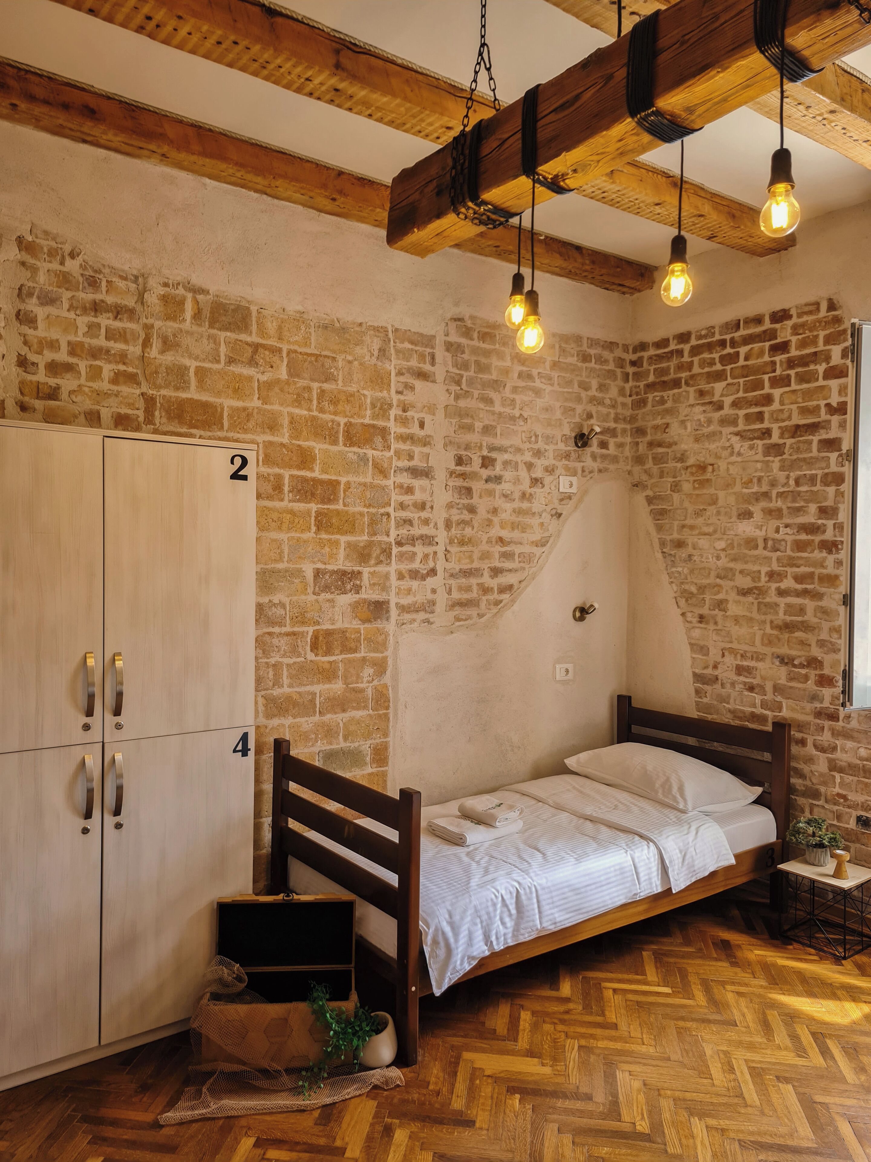 A room with a wooden bed, a brick wall, and a wooden wardrobe.