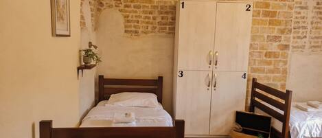 Quarto com cama de madeira, guarda-roupa de quatro portas, prateleira pequena com uma planta e chão de madeira em padrão herringbone.