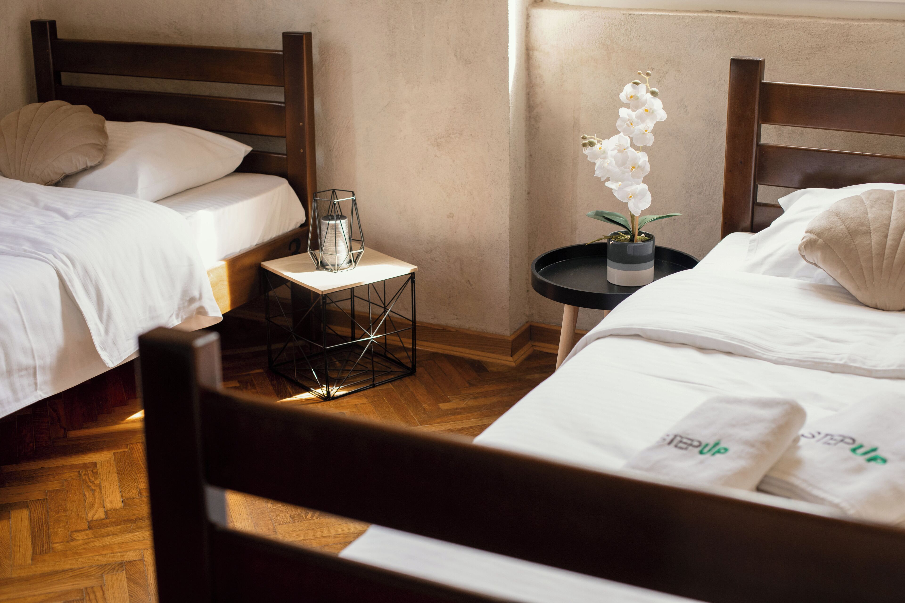 Una camera d'albergo con due letti, un tavolino con una lampada e un'orchidea in vaso.