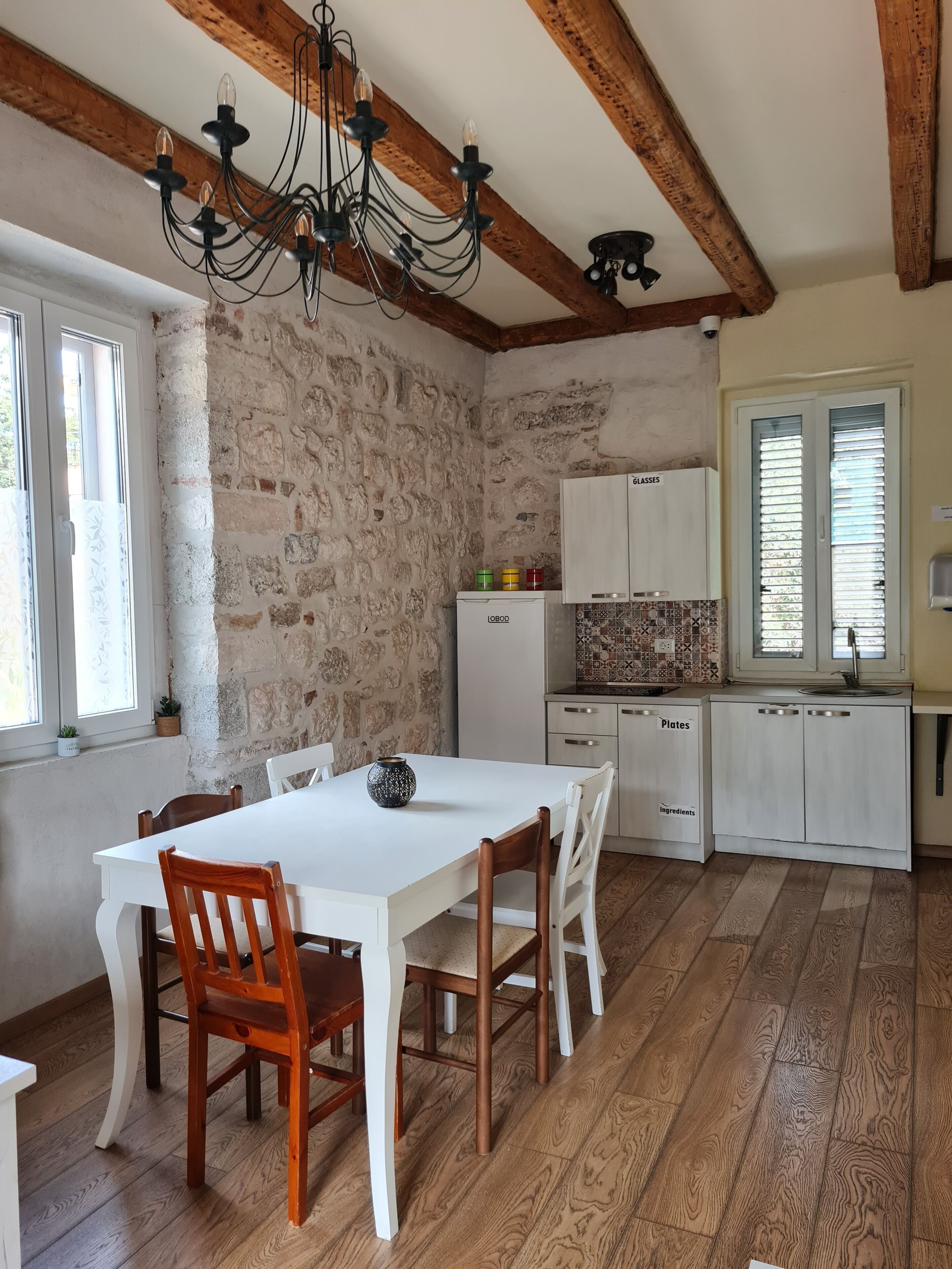 A dining area with a white table and wooden chairs, a stone wall, and a wooden ceiling.