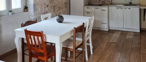 A dining area with a white table and wooden chairs, a stone wall, and a wooden ceiling.